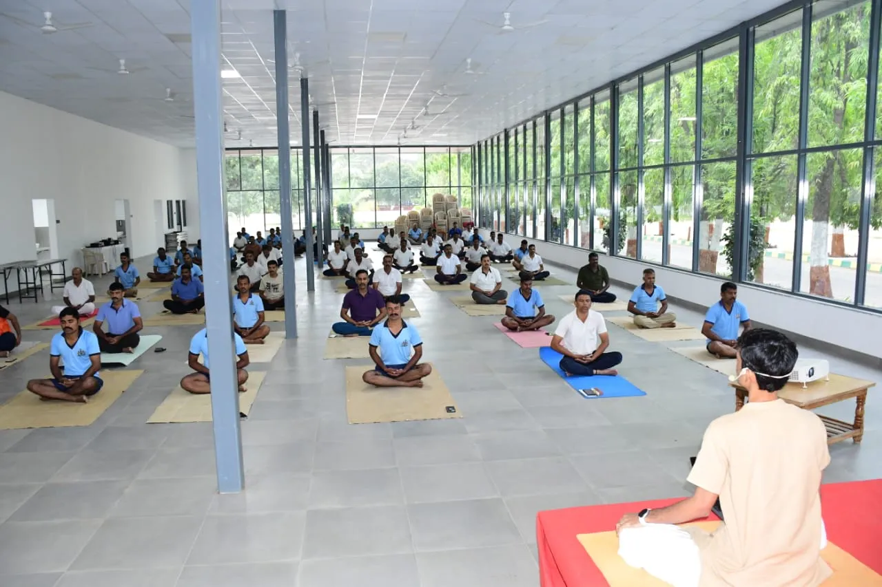 Shrungar teaching a hall of Karnataka State Reserve Police personnel, all seated on mats